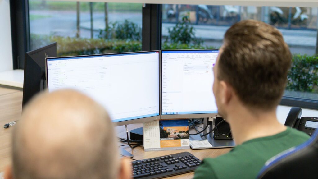 Medewerker achter twee beeldschermen op kantoor voor ISO 27001 informatiebeveiliging in de ICT en communicatie branche
